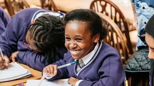 Young female pupil smiling and writing at a First Story workshop in Oxford