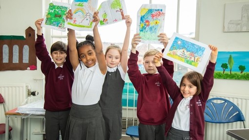 Children looking happy holding up drawings above their heads in a classroom setting 